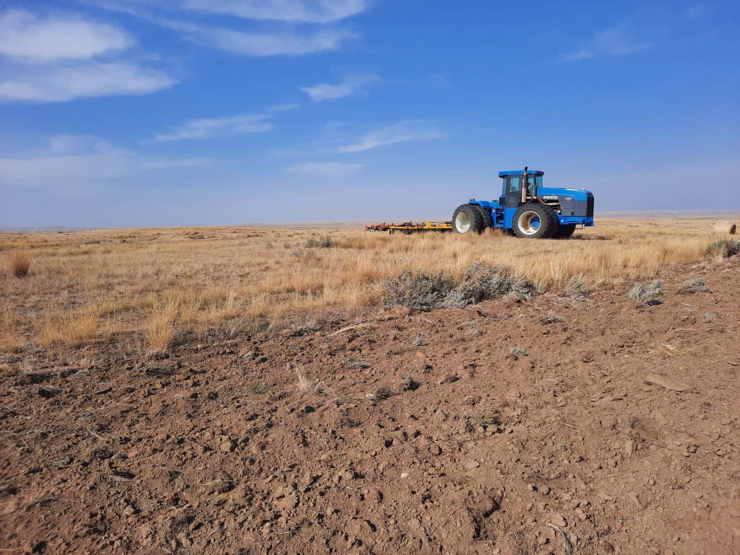 Image of tractor between plowed up field and native rangeland.